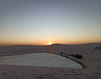 Dunas e lago com sol se pondo ao fundo