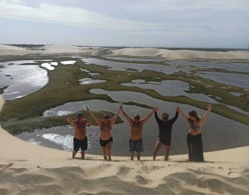 Pessoas tirando foto em uma duna com as mãos pra cima