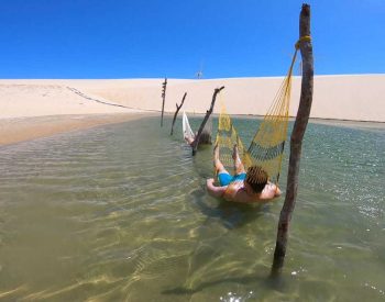 Duas pessoas relaxando em duas redes em uma lagoa entre as dunas